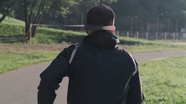 Spor adamı parkta koşuyor. Açık havada egzersiz kardiyo egzersiz. Yavaş çekimde güneşli parkta koşan genç adamın geri görünümü