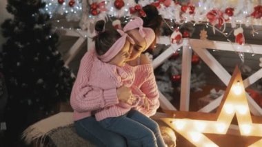 Mutlu anne Noel ağacı yakınında onun çocuk kızı ile eğleniyor. Pembe pullovers güzel anne ve kızı. Anne yavaş çekimde küçük kızını gıdıklıyor. Annelik kavramı. Orta atış