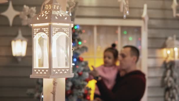 スローモーションでぼやけた背景にクリスマスと新年の木を飾る父と娘 ミディアムショット 前景のランタン — ストック動画