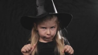 Siyah elbiseli ve şapkalı küçük güzel bir cadı karanlık arka planda bağırıyor. Cadılar Bayramı konsepti. Yakın çekim portre