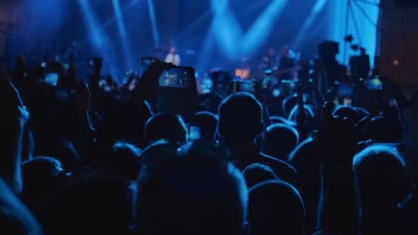 夜のロックコンサートで手を拍手するコンサートの大観衆 観客のシルエットの手は コンサートを楽しんでスマートフォンを使用しています ウード — ストック動画