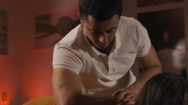 Erkek masör sıcak ortam ışığında masaj masasında genç kadın profesyonel masaj yapıyor. Güzellik bakımları. Orta atış. 4k, Uhd