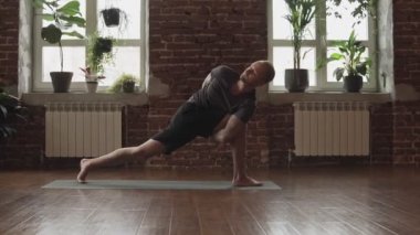 Adam uygulama yoga tuğla duvar ile stüdyoda poz. Spor salonunda yavaş çekimde yoga pozu alan genç adam. Fitness ve sağlıklı yaşam tarzı kavramı.