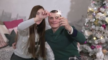 Mutlu aile evde Noel sırasında Kıvılcım ile eğlenmek. Gülümseyen adam ve kadın Noel ağacının yanında kucaklıyorlar. Orta atış