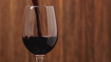 Sağda copyspace ile kadehiçine kırmızı şarap dökme yavaş hareket. Kırmızı şarabın yakın çekimi camda güzel bir dalga oluşturur. Ahşap arka planda cam dökülen şarap.