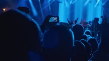 Seyircilerin siluet elleri insanlar konserden keyif alırken akıllı telefonlar kullanıyorlar. Konserde büyük bir kalabalık alkışlıyor. Gece rock konserinde el çırpıyorlar. 4k, UHD