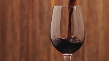 Soldaki copyspace ile kadehiçine kırmızı şarap dökme yavaş hareket. Kırmızı şarabın yakın çekimi camda güzel bir dalga oluşturur. Ahşap arka planda cam dökülen şarap.