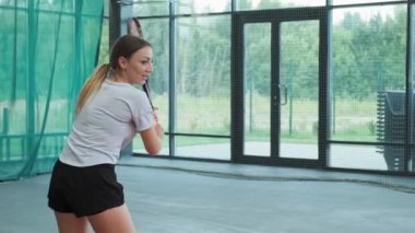 Spor giyimli kadın içeride tenis oynuyor. Mavi gömlekli sportif kadın yavaş çekimde tenis oynuyor. Orta oyuncu atışı. Spor konsepti