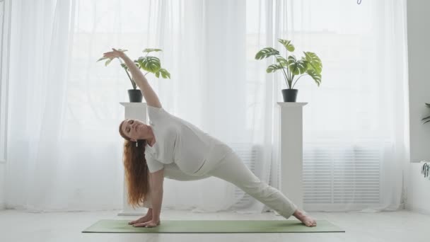 Donna incinta attiva. Bella rossa incinta che fa yoga sul pavimento a casa . — Video Stock