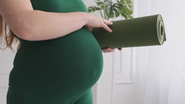 Nahaufnahme von Schwangerschaftsbauch und Frauenhand, die eine Yogamatte hält. Gesundheitskonzept — Stockvideo