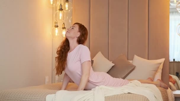 Χαλαρή νεαρή γυναίκα με πιτζάμες που τεντώνεται στο κρεβάτι στο υπνοδωμάτιο. Κοκκινομάλλα 30άρα — Αρχείο Βίντεο