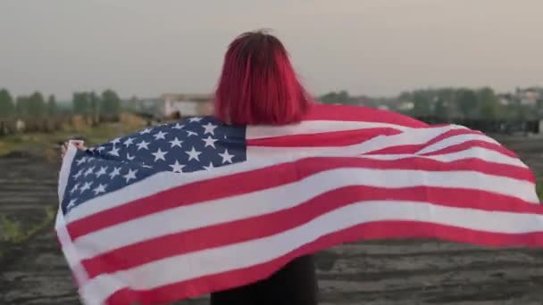 Ελκυστική νεαρή γυναίκα με σημαία των ΗΠΑ που περπατάει στην οροφή. Ημέρα ανεξαρτησίας των ΗΠΑ. — Αρχείο Βίντεο