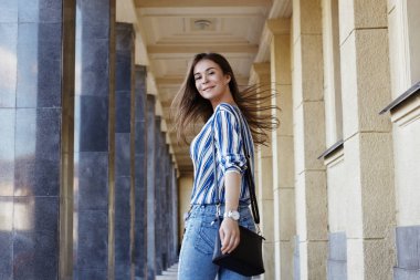 Happy Woman. Street Style Outdoors Portrait of Beautiful Girl. Young Woman Smiling. She wearing Print Shirt, Blue Jeans and Black Bag. Happy Lifestyle shoot clipart