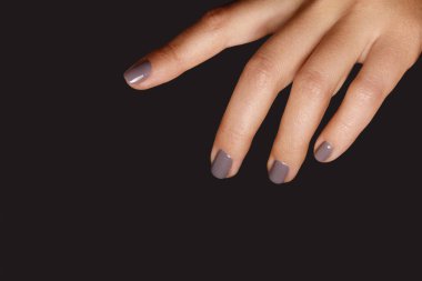 Closeup of female hand with short nails and fashion grey manicure in coffee shade on dark backdrop. Professional Nail art perfect for Beauty Salon, Nail Artist, Cosmetic Store concepts.