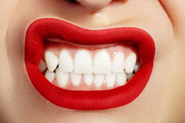 Macro beauty of open mouth shows a grin white teeth and fashion creative lip make-up. Bright red lipstick on lips. Whitening in stomatology, cosmetology and correction of teeth.