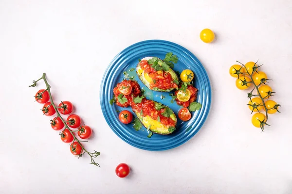 Bir avokado içinde pişmiş ve domates sosu, zeytin yağı ile hizmet yumurta ve taze organik Salantro sarı ve kırmızı içinde yarım dilimlenmiş domates ile dekore edilmiştir. Üstten görünüm