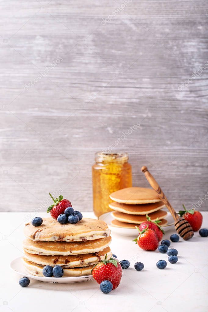 Blueberry pancakes served with strawberries and blueberries over white background. Copy space
