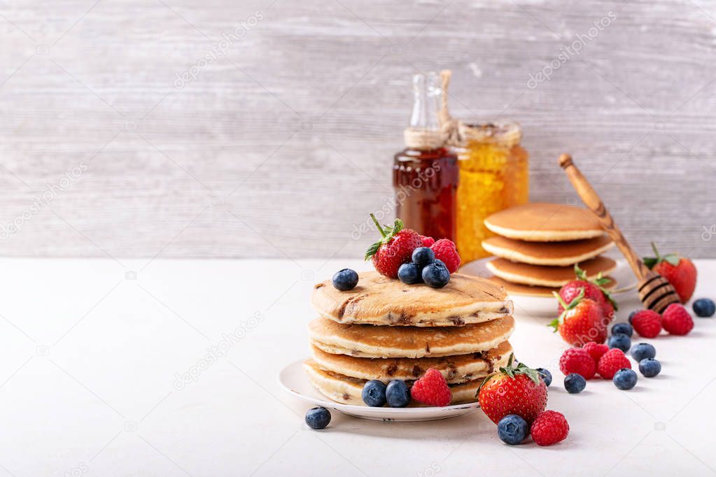 Blueberry pancakes served with strawberries, blueberries, raspberries, honey and maple syrup over white background. Copy space