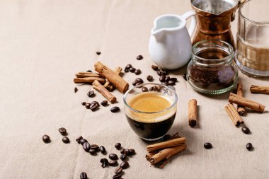 Kahverengi kumaş arka planında tarçın çubukları olan cam bardaklarda taze kahve. Üst manzara, düz uzanma