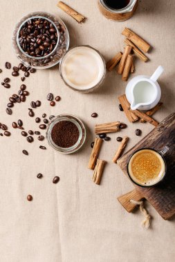 Kahverengi kumaş arka planında tarçın çubukları olan cam bardaklarda taze kahve. Üst manzara, düz uzanma