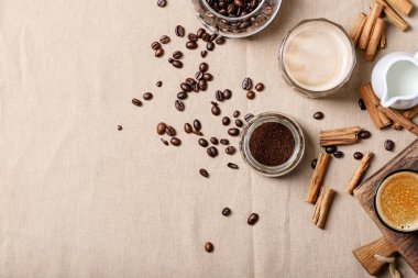 Kahverengi kumaş arka planında tarçın çubukları olan cam bardaklarda taze kahve. Üst manzara, düz uzanma