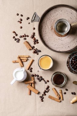 Kahverengi kumaş arka planında tarçın çubukları olan cam bardaklarda taze kahve. Üst manzara, düz uzanma