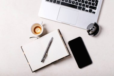 Not defteri, kalem, akıllı telefon, dizüstü bilgisayar ve beyaz arka planda bir fincan kahve olan bir çalışma yeri. Üst manzara, düz yatış. Uzayı kopyala Kavram