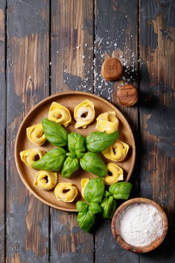 Koyu ahşap zemin üzerinde fesleğen ve un bulunan çiğ İtalyan mantısı. Üst manzara, düz yatış. Boşluğu kopyala