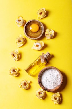 Çiğ İtalyan mantısı un, yumurta ve tuz ile ahşap tahtada parlak sarı arka planda. Üst manzara, düz uzanma