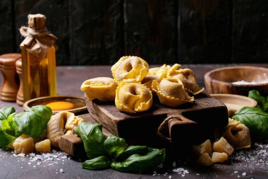 Çiğ İtalyan mantısı un, fesleğen, yumurta ve tuz ile ahşap tahtada kahverengi doku arka planında.