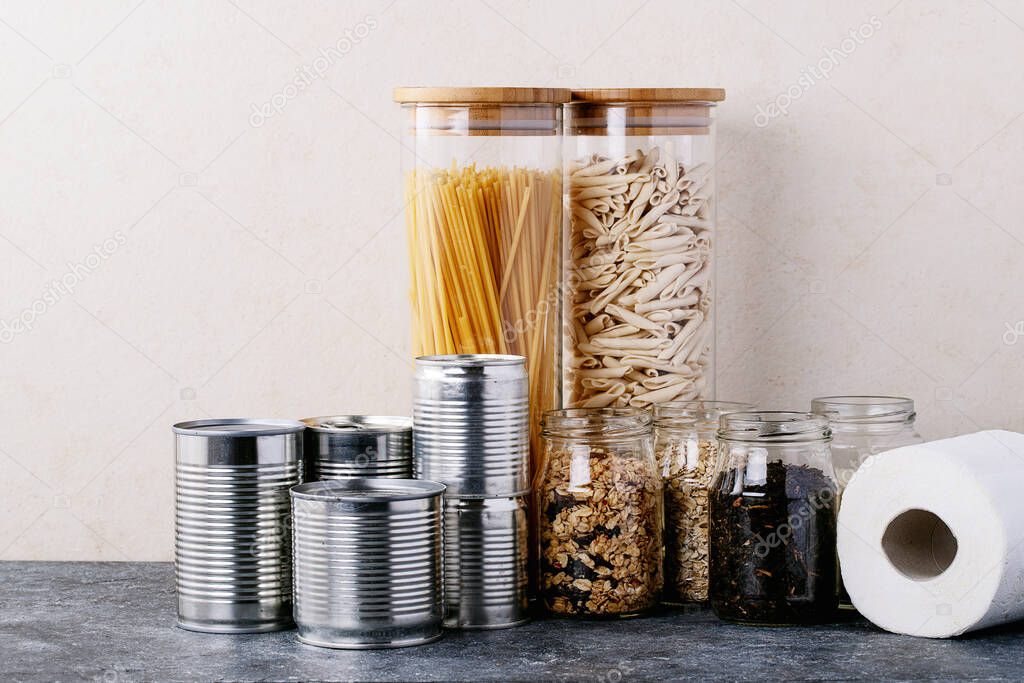 Canned food in metal cans with oats, rice, tea, and pasta in glass jars over white texture background. Copy space. Food supply concept