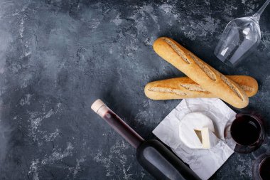 Bir bardak kırmızı şarap, peynirli camembert peyniri ve koyu dokuda Fransız ekmeği. Üst manzara, düz yatış. Boşluğu kopyala