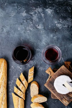 Bir bardak kırmızı şarap, peynirli camembert peyniri ve koyu dokuda Fransız ekmeği. Üst manzara, düz yatış. Boşluğu kopyala