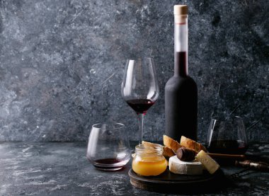 Bir bardak kırmızı şarap, peynirli camembert peyniri, bal, reçel ve Fransız ekmeği ile servis edilir.