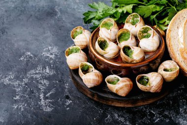 Sarımsaklı tereyağlı fırında salyangoz ve seramik tavada taze otlar koyu tekstil arka planında.