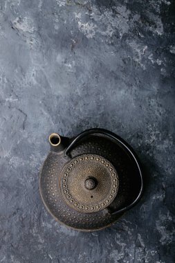 Siyah metal çaydanlık ve koyu dokuda gül yapraklarıyla seramik bir fincanda siyah ve yeşil çay. Üst Manzara. Boşluğu Kopyala