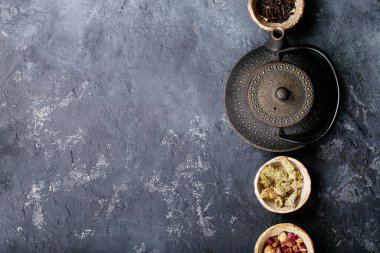 Siyah metal çaydanlık ve koyu dokuda gül yapraklarıyla seramik bir fincanda siyah ve yeşil çay. Üst Manzara. Boşluğu Kopyala