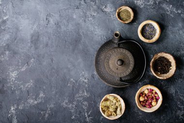 Siyah metal çaydanlık ve koyu dokuda gül yapraklarıyla seramik bir fincanda siyah ve yeşil çay. Üst Manzara. Boşluğu Kopyala