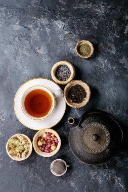 Siyah metal çaydanlık ve koyu dokuda gül yapraklarıyla seramik bir fincanda siyah ve yeşil çay. Üst Manzara. Boşluğu Kopyala