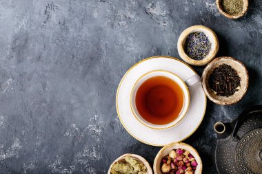 Siyah metal çaydanlık ve koyu dokuda gül yapraklarıyla seramik bir fincanda siyah ve yeşil çay. Üst Manzara. Boşluğu Kopyala