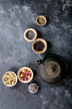 Siyah metal çaydanlık ve koyu dokuda gül yapraklarıyla seramik bir fincanda siyah ve yeşil çay. Üst Manzara. Boşluğu Kopyala