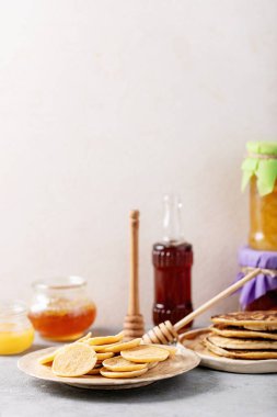 Bal, akçaağaç şurubu ve beyaz arka planda reçel ile servis edilen bir yığın sade mini krep..