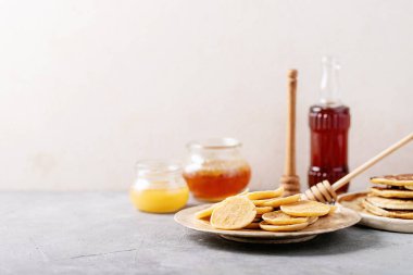 Bal, akçaağaç şurubu ve beyaz arka planda reçel ile servis edilen bir yığın sade mini krep..