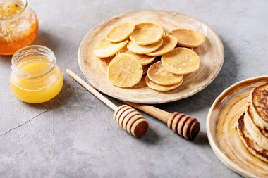 Beyaz arka planda bal ile servis edilen bir yığın sade mini krep..