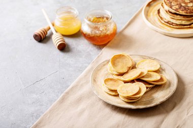 Beyaz arka planda bal ile servis edilen bir yığın sade mini krep..