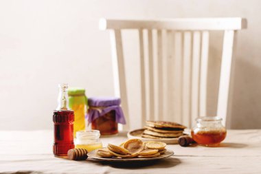 Bal, akçaağaç şurubu ve beyaz arka planda reçel ile servis edilen bir yığın sade mini krep..