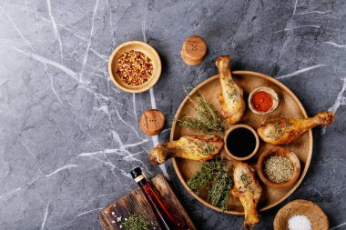 Izgara acılı tavuk budu, taze kekik, tuz, acı biber taneleri, kekik ve barbekü sosu ile koyu dokuma arka planda. Üst manzara, düz yatış. Boşluğu kopyala