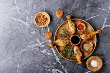 Izgara acılı tavuk budu, taze kekik, tuz, acı biber taneleri, kekik ve barbekü sosu ile koyu dokuma arka planda. Üst manzara, düz yatış. Boşluğu kopyala