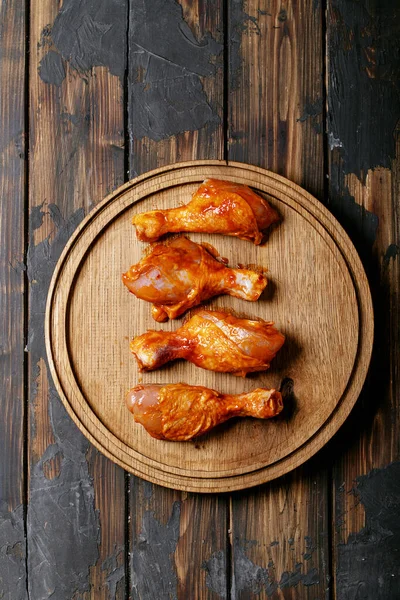 Raw chili chicken drumsticks with fresh thyme, salt, chili flakes, oregano and barbecue sauce over dark wooden background. Top view, flat lay. Copy space