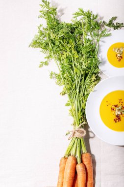 Seramik tabakta havuç püresi çorbası ve koyu dokuda taze organik havuç. Üst manzara, düz yatış. Boşluğu kopyala